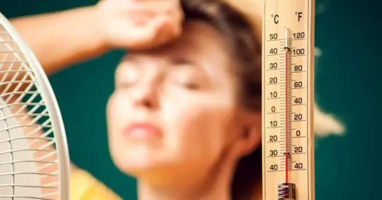Woman in front of fan suffering from heat holding thermometer