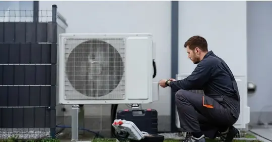 Technician servicing outdoor air source heat pump unit near house wall